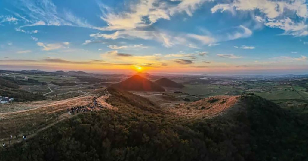 아직 푸른 초록빛의 오름과 주변 제주 서부 평야, 그리고 멀리 보이는 바다까지 담긴 장면